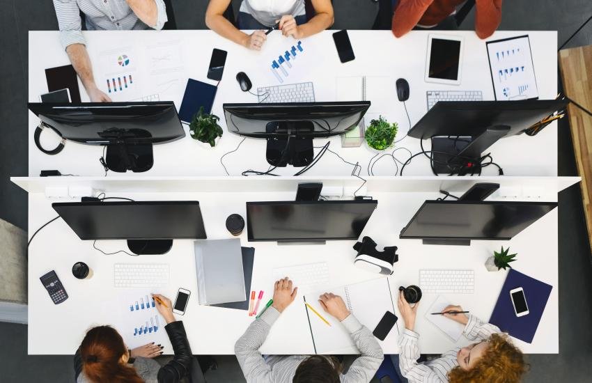 Mesa de trabajo en la cual laboran seis personas, vista desde arriba.